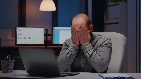 Overworked Businessman Rubbing Face While Working at Financial Statistics