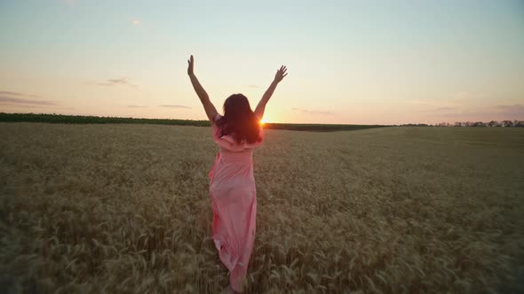 A Girl in a Dress Runs Through a Wheat Field at Sunset