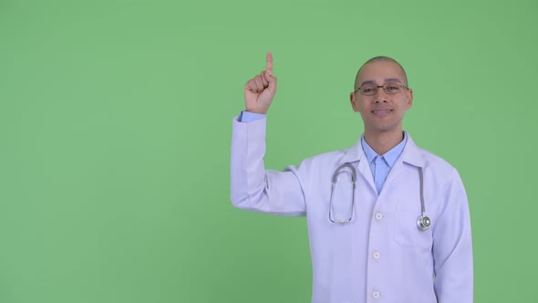Happy Bald Multi Ethnic Man Doctor Pointing Up and Giving Thumbs Up