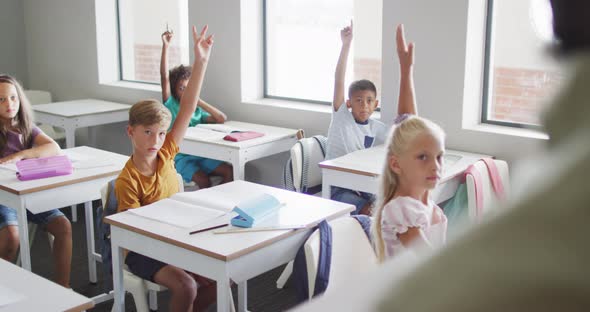 Video of diverse pupils raising hands during lesson in classsroom