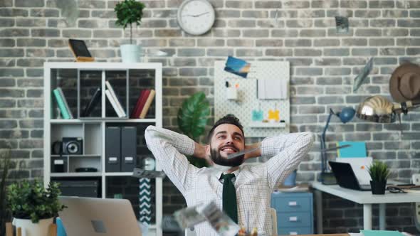 Slow Motion of Cash Falling on Excited Entrepreneur Sitting at Table in Office