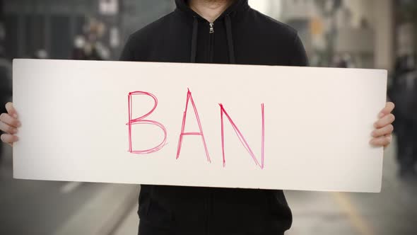 Unknown Activist Holds a Placard with BAN Text