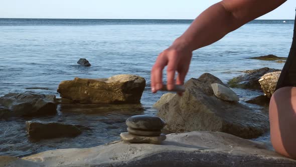 Young Woman in Black Swimsuit Stacking Stones at Rocky Coast