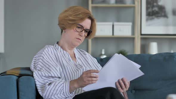 Old Woman Reading Documents while Sitting on Sofa