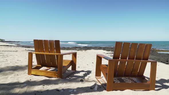 Empty wooden beach chairs facing waves on a pristine white sand Hawaiian island