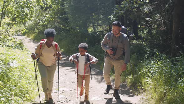 Happy Multiethnic Family Walking with Trekking Poles and Backpacks