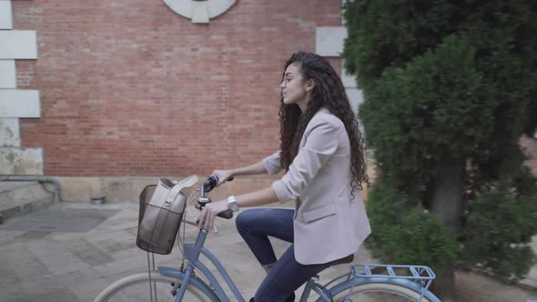 Moroccan Girl Wearing A Coat Biking Towards City Fountain