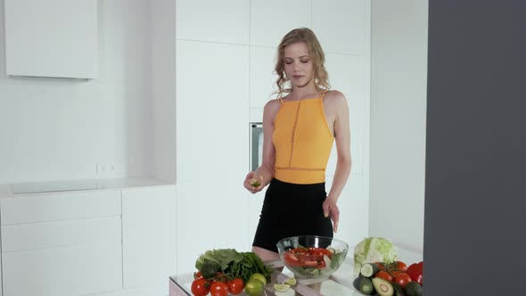 Young Woman Presses Lime Juice On Vegetable Salad. White Modern Kitchen.