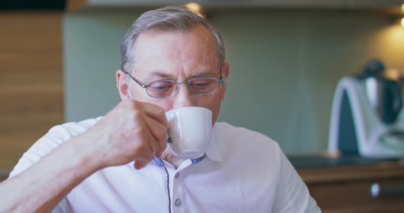 Delicious Drink Pleasant Elderly Man in Spectacles Sitting on Chair in Kitchen