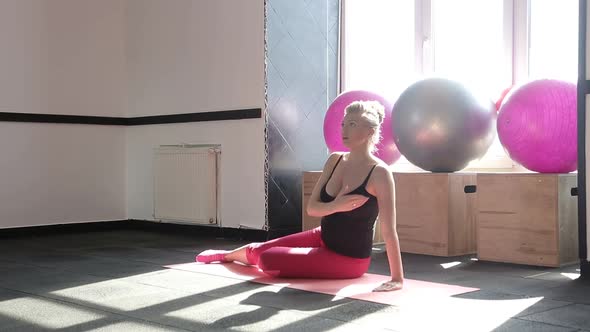 Pregnant Woman Sitting on Yoga Mat and Performs Warmup on White Background