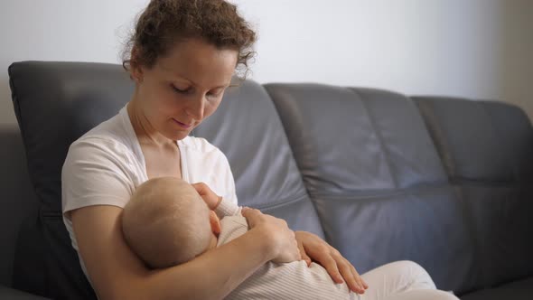 Mother Breastfeeding Small Girl on Sofa at Home