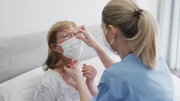 Female health worker putting face mask on senior woman at home