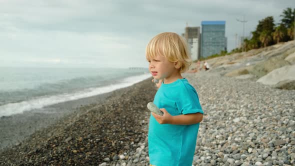 A Little Boy is Playing on the Seashore He Throws Stones Into the Water