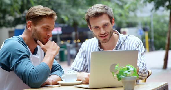 Friends discussing over laptop while having coffee in cafe 4k