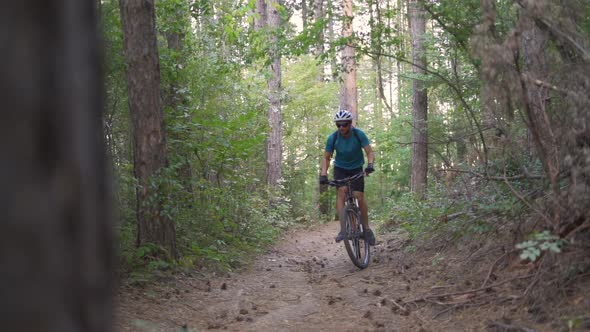 Young Mountain Biker Climbs on a Path in a Forest