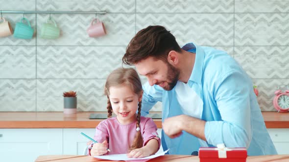 Father teaching little daughter to write at the kitchen table at home