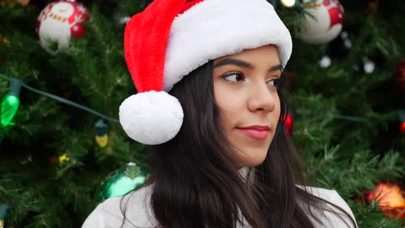 A beautiful hispanic woman in a Santa hat celebrating the merry holiday season with a Christmas tree