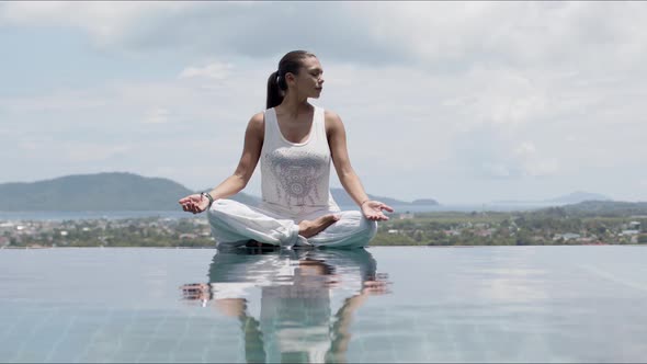 Serene Woman Practicing Yoga in Lotus Posture Poolside Against Sky