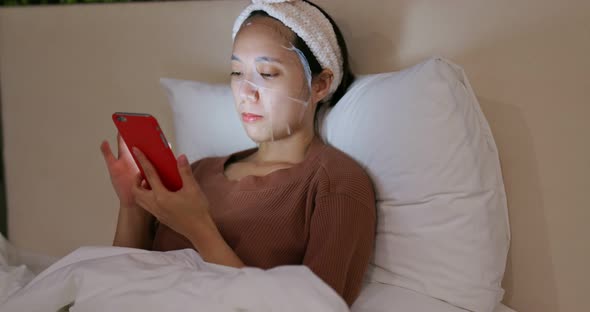 Woman apply paper mask and watch on cellphone at home