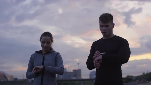 Young Sportive Couple Using Smartwatches and Running Outdoors