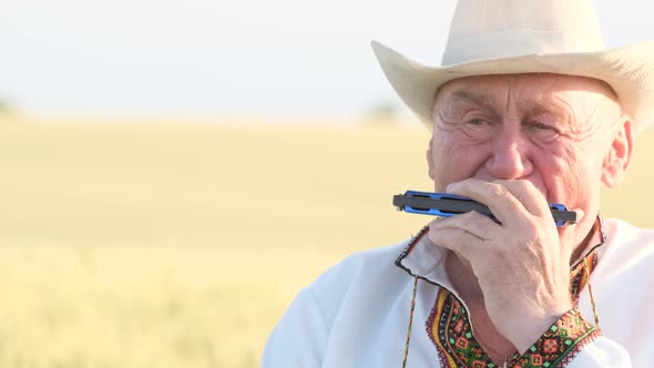 Closeup of the Face of an Old Man in a Hat Playing the Harmonica