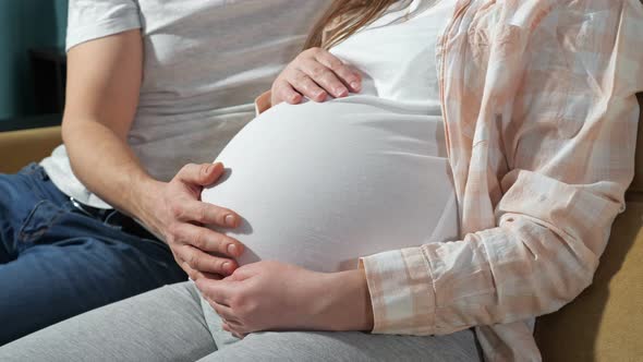 Couple Family Future Expecting Parents Sitting on Couch Man Stroking Wife's Pregnant Belly with Cute