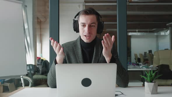 Smiling Businessman in Headphones Using Laptop Computer for Video Conference While Sitting at Office