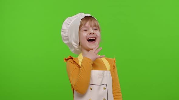 Child Girl Dressed Cook Chef Baker in Apron and Hat Laughing Out Loud After Hearing Funny Joke