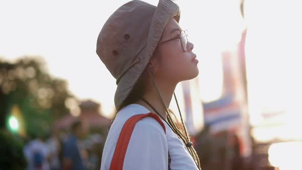 Young Asian woman looking around amusement park at sunset.