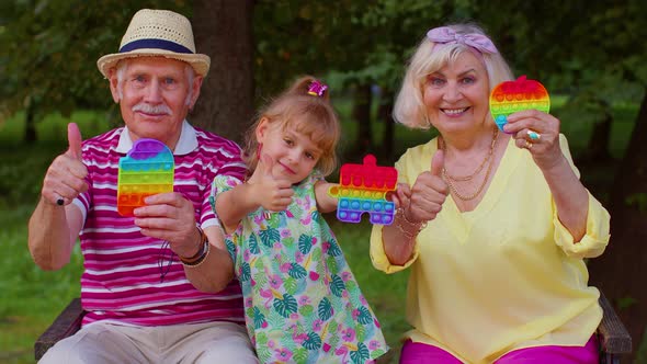 Smiling Senior Grandmother Grandfather with Granddaughter Playing Squeezing Antistress Toy Game