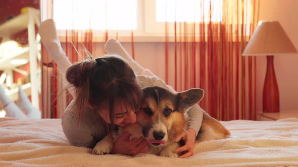 Closeup Portrait of Pleased Woman Lying on Bed at Home with Her Loved Dog Welsh Corgi