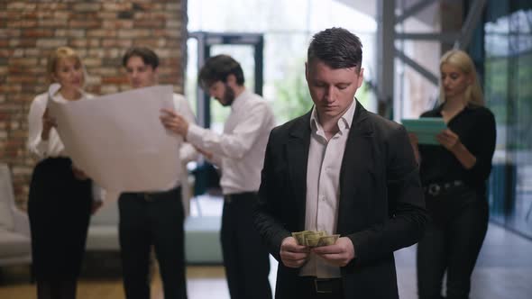 Caucasian Young Man Counting Money in Office Corridor Leaving in Slow Motion with Blurred Colleagues