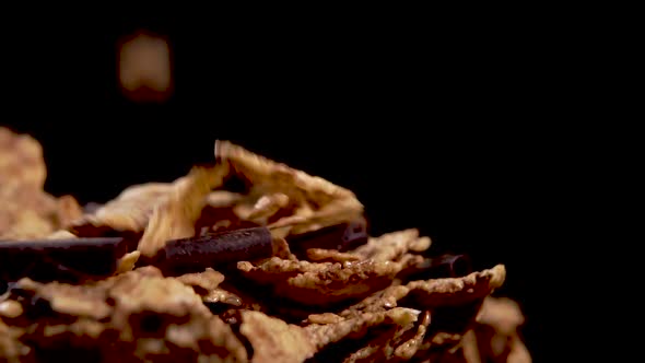 Dry wheat flakes with chocolate chips falling into a heap in a wooden bowl in slow motion. Macro