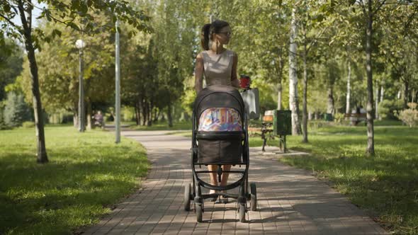 Wide Shot of Confident Elegant Businesswoman Strolling in Summer Park with Baby Carriage. Positive