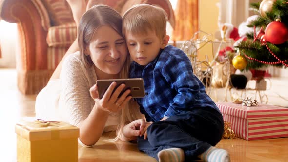 Video of Happy Smiling Fmaily Lying on Floor Under Christmas Tree and Using Smartphone