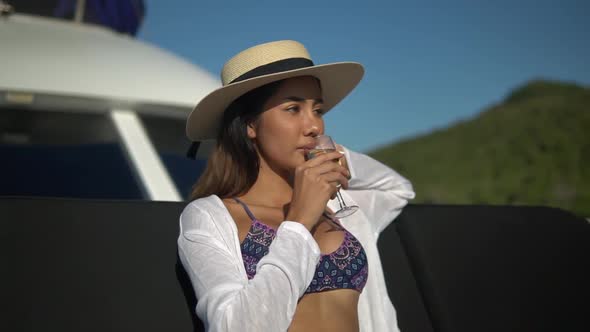 Beautiful Young Lady in a Straw Hat and Bikini Relaxing on Board of Yacht Drinking Champagne 