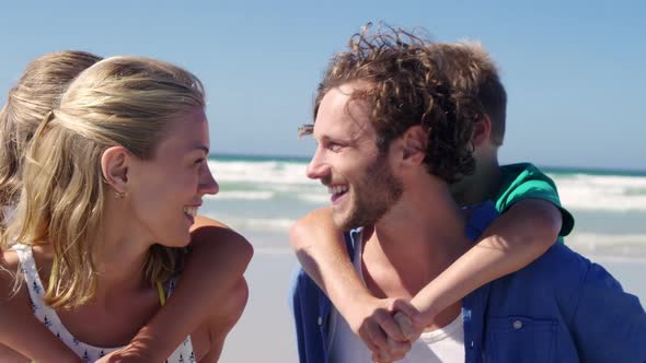 Parents giving piggyback ride to their children at beach