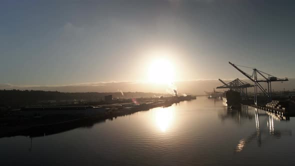 Golden sunlight reflecting off calm water, giant cranes unload containers from ships, aerial