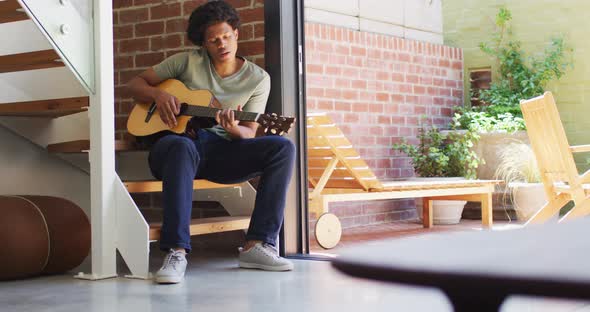 Happy african american man plays guitar and singing at home