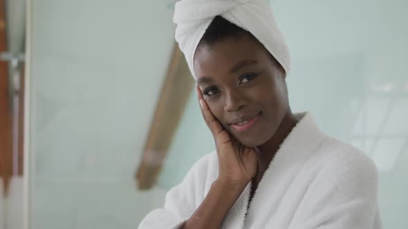 Portrait of smiling african american attractive woman wearing robe and turban in bathroom