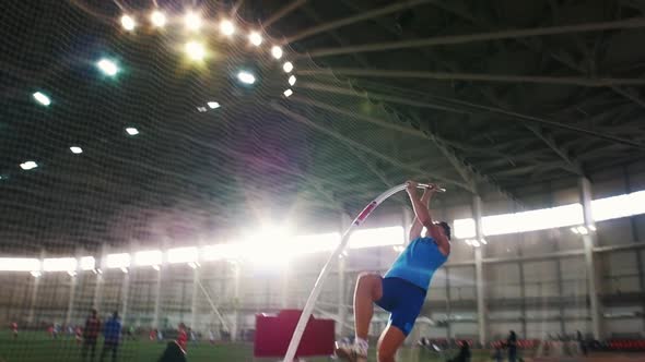 Pole Vault Training in the Stadium - a Young Man in Blue Shirt Jumping Over the Bar