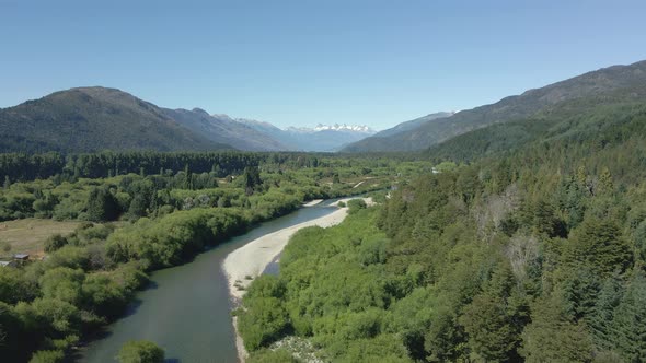 Aerial dolly in of Rio Azul stream between pine tree woods with mountains in background, Patagonia A