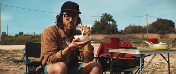 Young man eating from a bowl outdoors on camp site