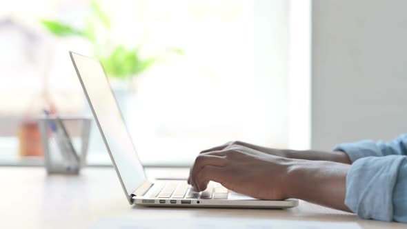 Side View of Young African Man Typing on Laptop Keyboard