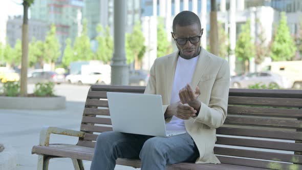 African Man with Wrist Pain Using Laptop While Sitting Outdoor on Bench