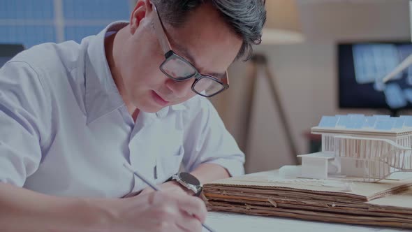 Close Up Of Asian Man Sketch House With Solar Panel On The Blueprint