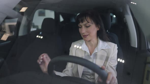 Shooting Via Windshield of Confident Slim Beautiful Woman Examining Car Interiors Sitting on Driver