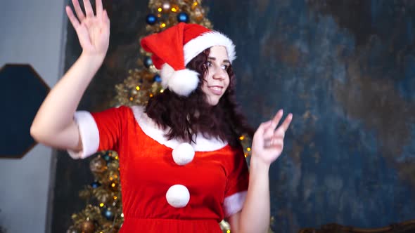 Young Woman in Santa Claus Costume Dancing on Background of Christmas Tree. Happy Female Resting and