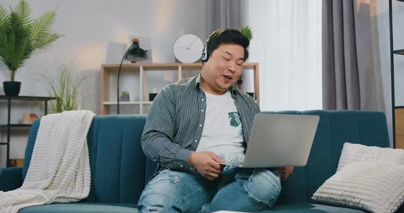 Asian Guy in Headset Enjoying His Video Call while Sitting on Comfortable Sofa