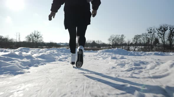 Professional female skater in white figure skates is skating on frozen lake